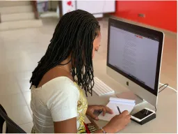 Woman sitting at desk and writing on notepad with a computer screen in front of her