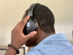 Side of man's head. He is holding black headphones on his head. His face is not visible